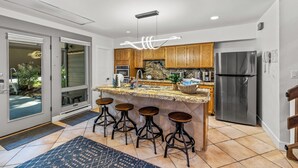 Una cocina moderna con una isla central, taburetes de bar, un refrigerador de acero inoxidable y armarios de madera.
