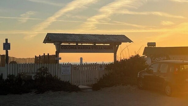 En strandpromenad med ett trästaket, en skylt med texten ”Colonia Marina Stella Maris” och ett fordon parkerat i närheten.