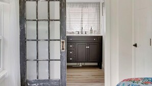 A room with a sliding door leading to a bathroom, a bed with a floral bedspread, and a wooden floor. - Pet Friendly-Updated Goose Rocks Beach Oasis! (Kennebunkport)
