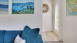 A living room with a blue sofa, two framed pictures of coastal scenes, a sunburst mirror, and a map on the wall. - Pet Friendly-Updated Goose Rocks Beach Oasis! (Kennebunkport)