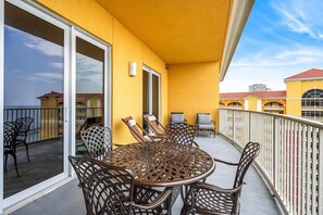 Ein Balkon mit rundem Tisch und Stühlen, eine Glastür und Blick auf Gebäude im Hintergrund.