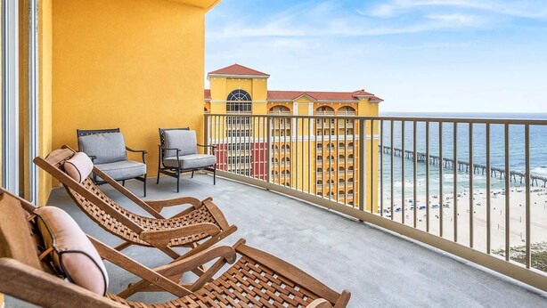 A balcony with wooden lounge chairs and a view of the beach and pier. - Salt and Shore Escape Sleeps 7 (Panama City Beach)
