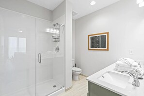 Een moderne badkamer met een douchecabine van glas, een wit wastafelmeubel met spiegel en een toilet.