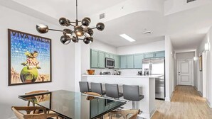 A modern kitchen with green cabinets, a central island, and a dining area with a glass table and wooden chairs. - Salt and Shore Escape Sleeps 7 (Panama City Beach)