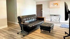 A living room with a black leather sofa, an ottoman, a ceiling fan, a wooden coffee table, and a TV stand with a flat-screen TV. - Upgraded entire residential home (Scottsdale)