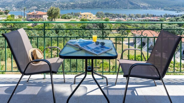Un balcon avec deux chaises et une table, donnant sur un lac et des montagnes.