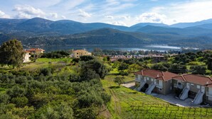 Une propriété située sur une colline, avec un vignoble, un petit bâtiment doté d’un toit rouge et un lac en arrière-plan.