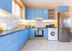 A modern kitchen with blue cabinets, a stainless steel refrigerator, a washing machine, and a coffee maker.