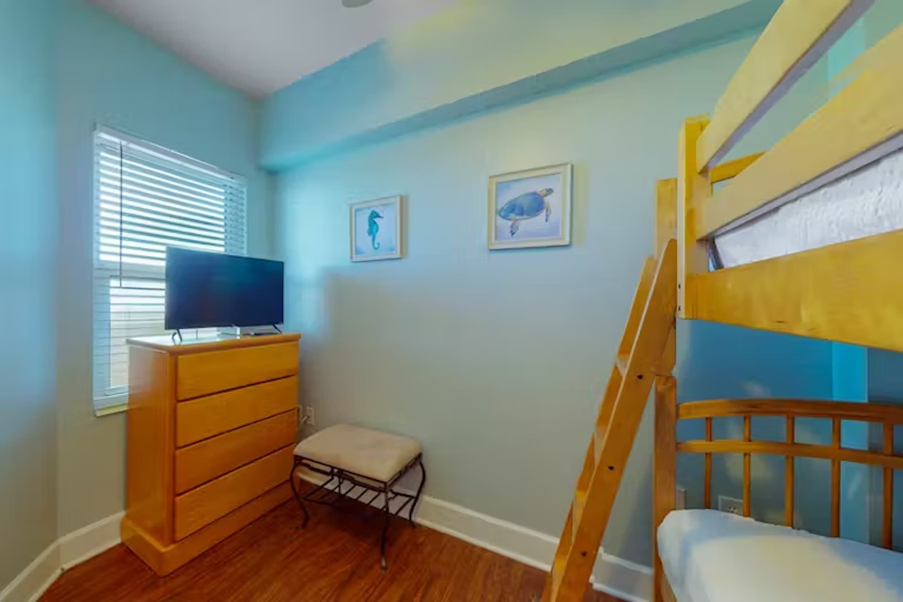 Un dormitorio infantil con una cama litera, un televisor en un tocador y dos cuadros en la pared.