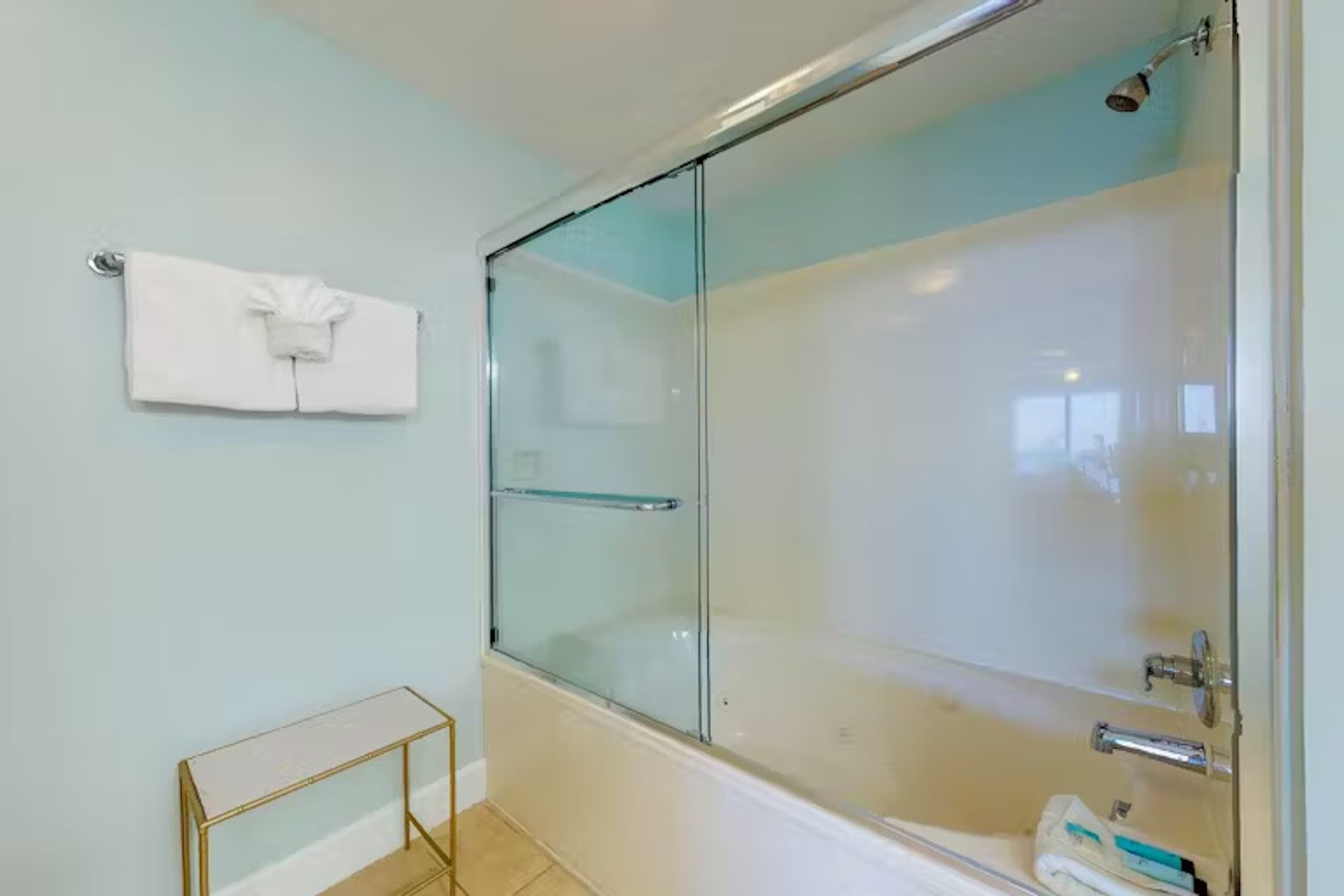 A modern bathroom with a glass-enclosed shower, a white bathtub, and a small gold-framed vanity table.
