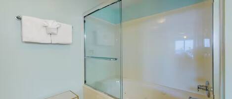 A modern bathroom with a glass-enclosed shower, a white bathtub, and a small gold-framed vanity table.