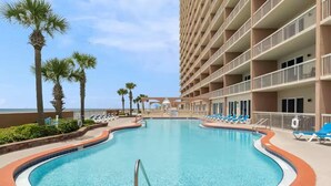 A swimming pool with a 3 FT depth marker, surrounded by lounge chairs and palm trees, with a building in the background. - Sunrise Serenity Resort Condo! (Panama City Beach)