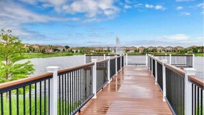 Una terraza de madera con barandillas que da a una masa de agua y una hilera de casas al fondo.