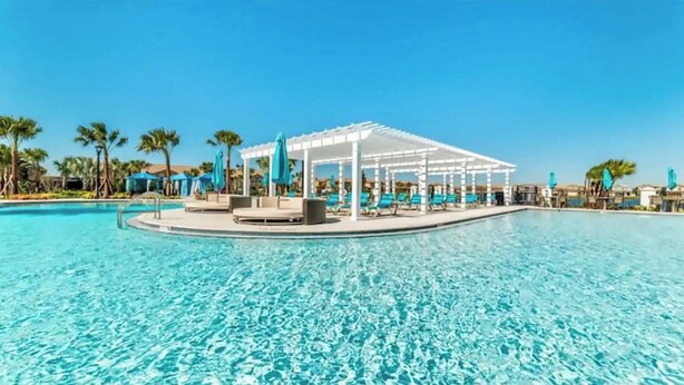Una piscina azul cristalina con un quiosco blanco y sillones de descanso.