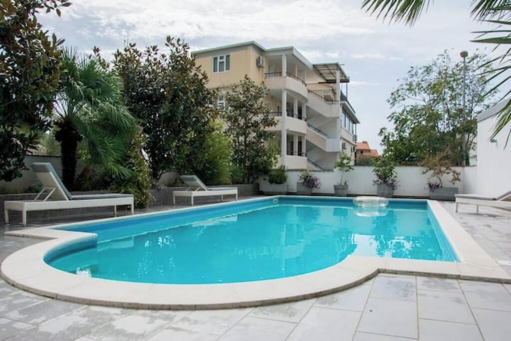 A swimming pool with a curved edge, surrounded by lounge chairs and potted plants.