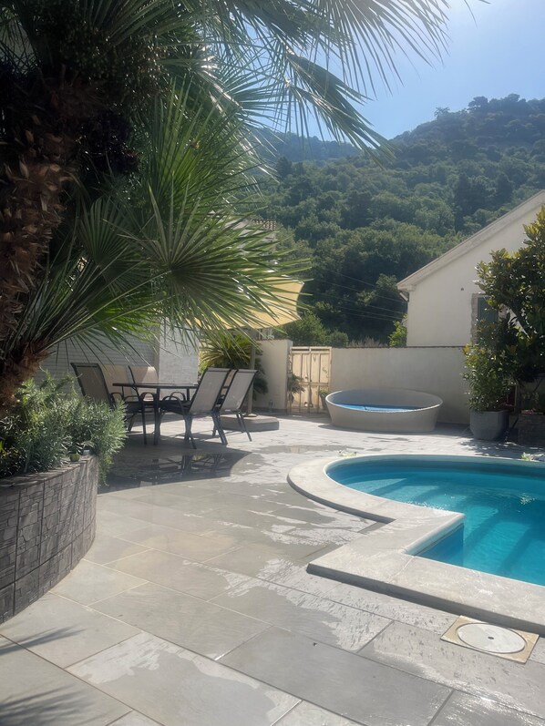 Zona de piscina con un patio de piedra, una mesa con sillas y vistas a una ladera.