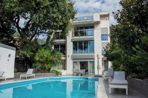 Un edificio moderno con piscina, rodeado de árboles y follaje.