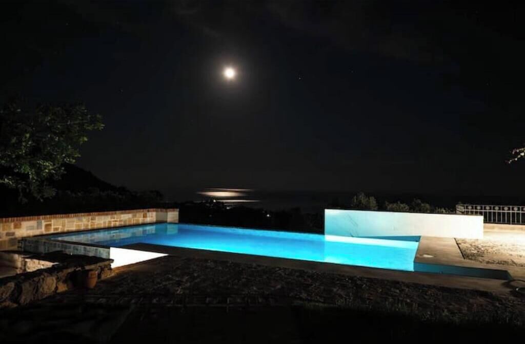 A nighttime swimming pool with a view of the moon and distant lights.