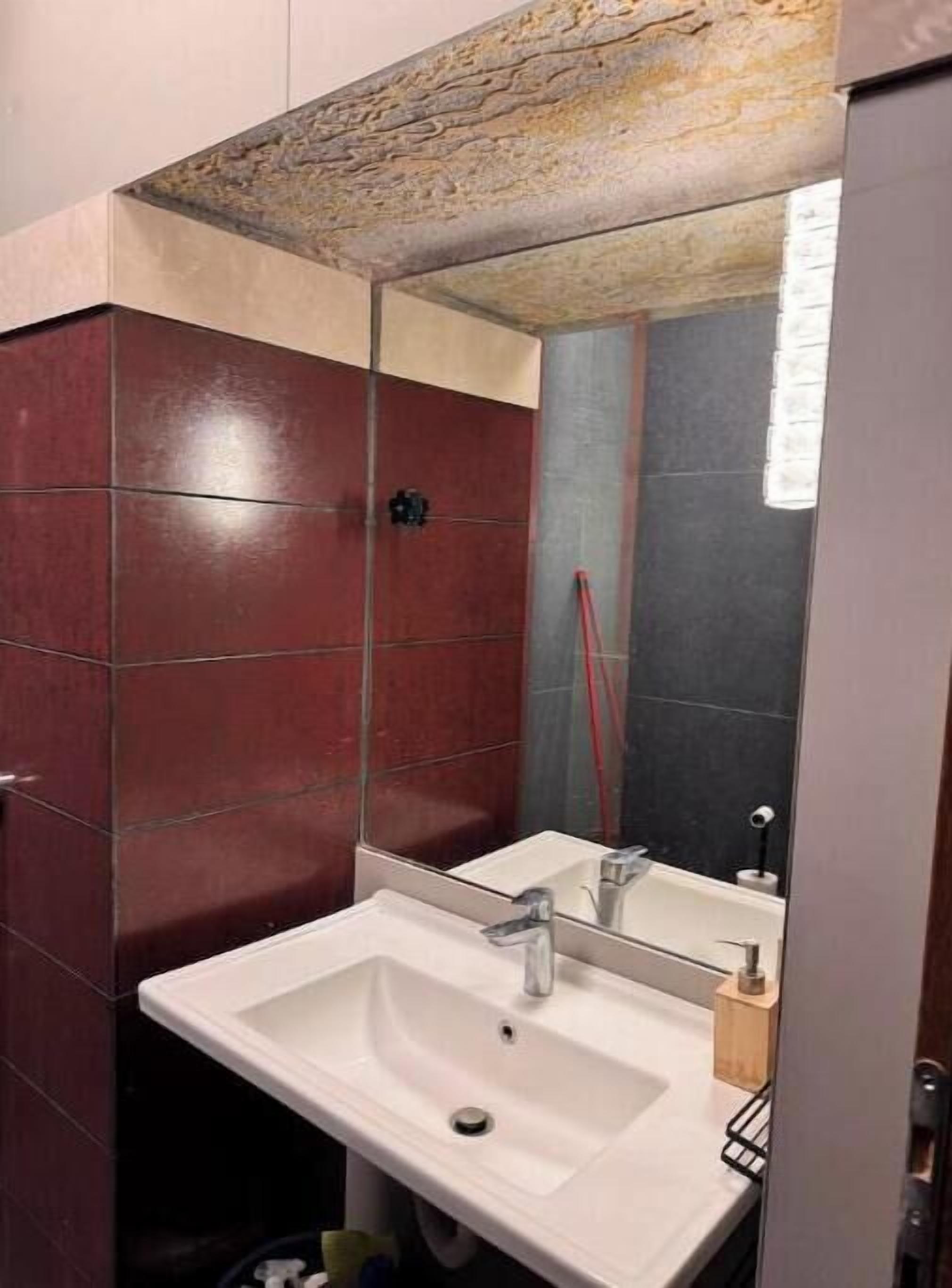 A bathroom with a white sink, a mirror, and red tiles.