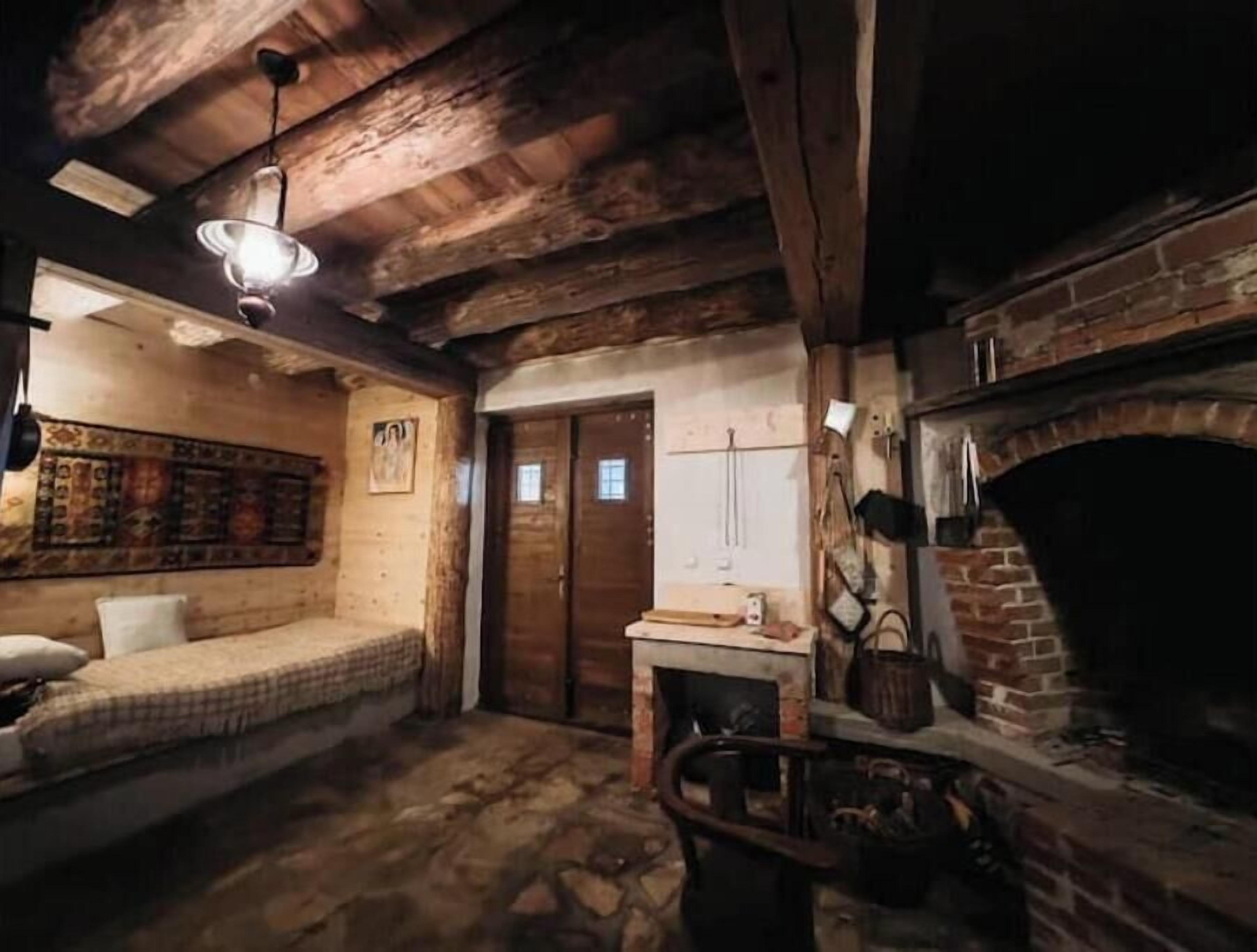 Une pièce rustique avec des poutres apparentes, un sol en pierre, un lit, une cheminée et un luminaire suspendu.
