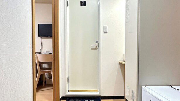 A hallway with a wooden floor, a door with a sign, a small table with slippers, and a refrigerator. - Airport line, Hanazonocho station 2 min. apartment, tourist attraction Namba Shinsaibashi 3 station excellent access [ 102]. (大阪市西成区花園北2丁目)