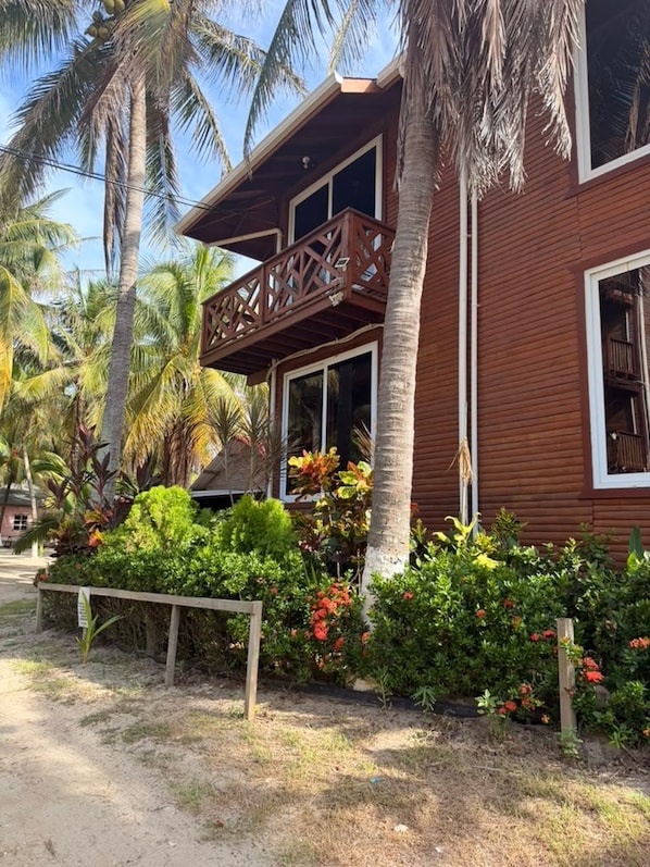 A wooden building with a balcony, surrounded by tropical vegetation and palm trees. - Oasis Paradise Hotel (Tela)