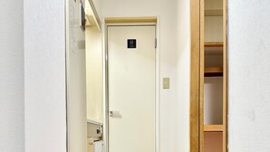 Un pasillo estrecho con suelo de madera, una puerta con un letrero que indica el baño de hombres y un felpudo con zapatos en el suelo.