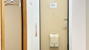Un pasillo con una puerta, un perchero, un portero automático en la pared y una caja de alarma contra incendios.