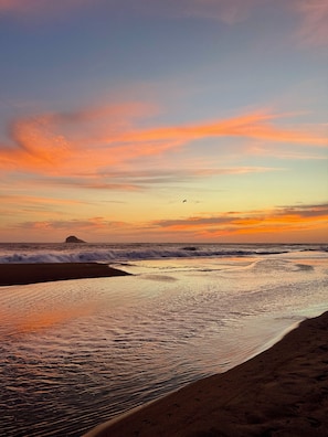A beach scene with waves, a distant island, and a clear sky.
