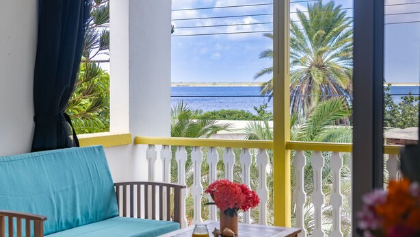 A balcony with a sofa, a small table, and a vase of flowers. - Divers Paradise 6, Divers paradise apartment with Ocean view!  (Kralendijk)