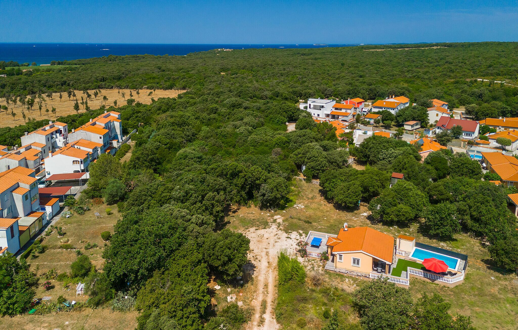 An aerial view of a coastal residential area with houses, a visible swimming pool, and a clear view of the sea.