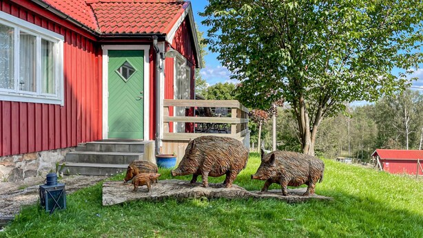Un edifici vermell amb una porta verda, un pont de fusta i tres escultures d'animals a l'herba.