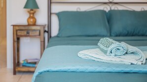 Una cama con ropa de cama color turquesa, una toalla enrollada y una mesita de noche con una lámpara.