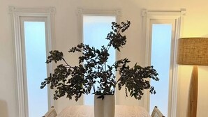 Une table à manger ornée d’un grand vase rempli de feuillage sombre, entourée de chaises en osier.