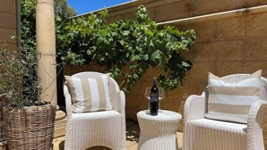 Une terrasse avec des meubles en osier et une bouteille de vin.