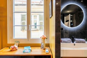 Ein Badezimmer mit einer Badewanne, einem runden Spiegel und einem Fenster mit Blick auf Gebäude.