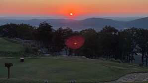 Solnedgang over et kuperet landskab med en golfbane i forgrunden.
