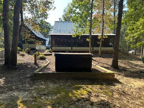 Uma cabana rústica com telhado de metal, rodeada por árvores e um jardim com hidromassagem.
