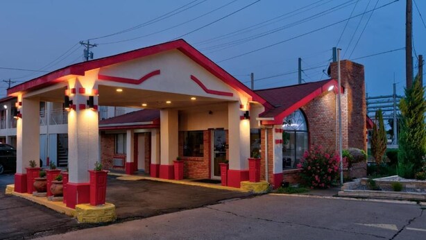 A motel with a red and white exterior, a covered parking area, and a brick building with a chimney.