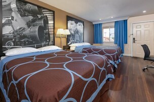 Habitación de hotel con dos camas, un cartel grande de un lanzamiento de cohete, un escritorio con una lámpara y vistas al exterior a través de una puerta.