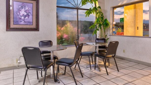 A dining area with a round table and four chairs, a framed picture on the wall, and a large window with a view of the sky and trees.