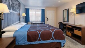 A hotel room with a large bed, a desk, a chair, a TV, and a bookshelf.