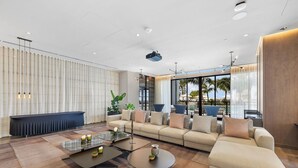 A modern living room with a sectional sofa, a coffee table, and a large window with a view of palm trees. - PH 51 - 1BD at NEW Worldcenter area + free parking (Miami)