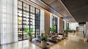 A spacious lobby with large windows, a seating area with sofas and armchairs, and several potted plants. - PH 51 - 1BD at NEW Worldcenter area + free parking (Miami)