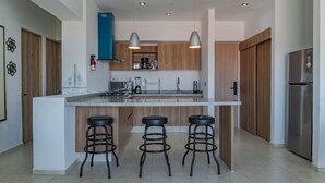 A modern kitchen with a central island, bar stools, stainless steel appliances, and wooden cabinetry.