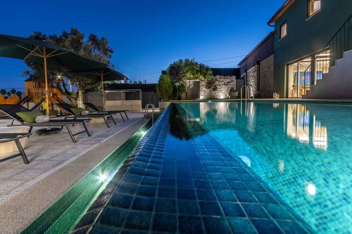 Una piscina amb gandules i ombrelles, una paret de pedra i un edifici amb una escala.
