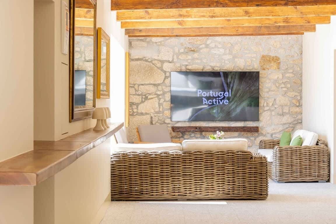 Un saló amb una paret de pedra, televisió de pantalla plana, mobles de vímet i sostre de fusta.