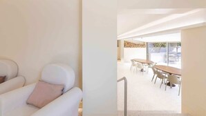 Et moderne interiør med en hvid sofa, et spiseområde med et træbord og stole, samt udsigt gennem en glasdør.