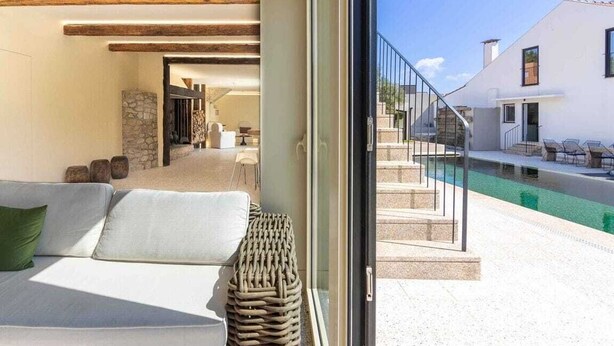 Et moderne interiør med sofa, fletkurv og udsigt til et udendørs poolområde.