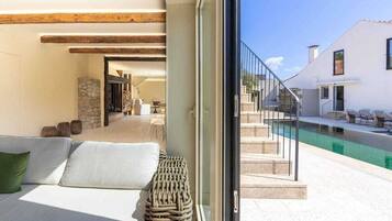 Un interior modern amb un sofà, cistella de vimet i vista a una zona de piscina exterior.
